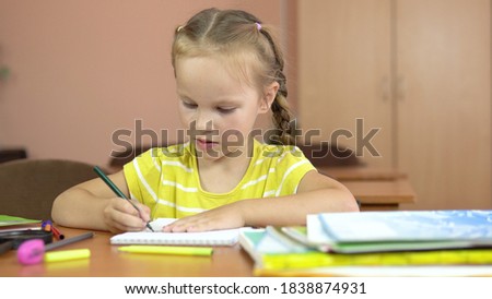 Little cute girl sits at a desk in the classroom. Draws in a notebook with a felt-tip pen. Preschool education. 4k