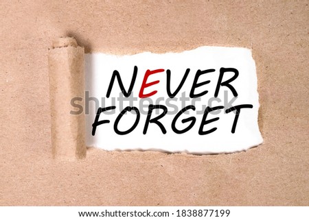 The text never forget appearing behind torn brown paper