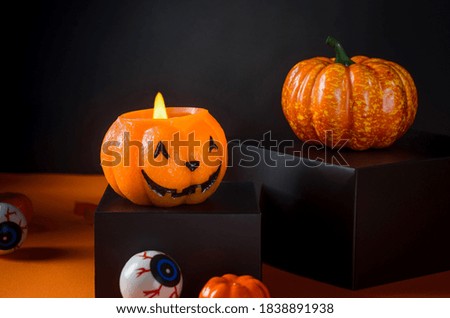 Halloween background with burning candle in the form of a pumpkin head jack lanter, decorative pumpkin, eyes, spiders on an orange background. 