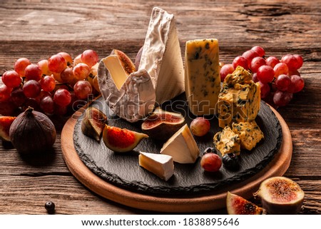 Delicious gourmet cheese, assortment of soft cheeses served with sliced sweet fresh figs and grapes on a rustic wooden background, catering, banner, menu, recipe, place for text.
