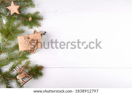 Christmas background, natural fir tree branches with wooden toys and craft gift on a white wooden background, horizontal new year web banner top view. Reusable sustainable recycled decor.