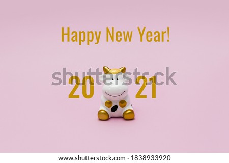 Words Happy New Year and toy Cow on pink background. White bull is the symbol of 2021 according to the Eastern calendar.
