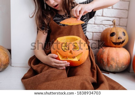 little girl with carving pumpkin on Halloween at home sitting next to fireplace in living room. Trick or treat. Child celebrating Halloween.