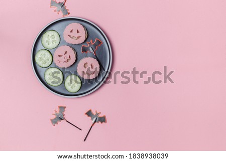 Appetizer for a Halloween party. A plate of ham Sandwiches with scary faces cut out. Top view on a pink background with space