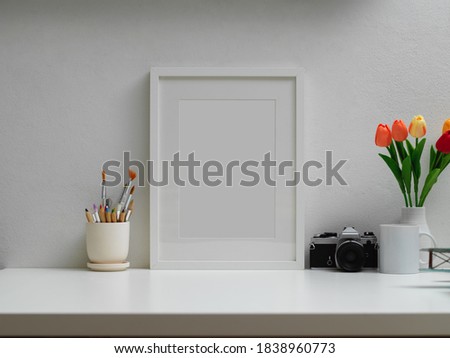 Cropped shot of home office with mock up frame, paint brushes, camera, flower vase and copy space