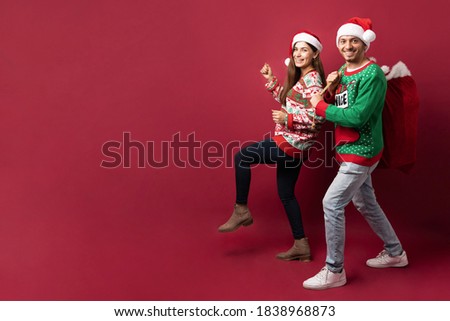 Full length view of a cute cheerful couple walking and carrying a sack with Christmas presents and delivering them