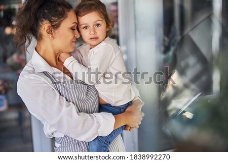 Waist-up photo of a beautiful brunette woman holding a cute little girl in her arms