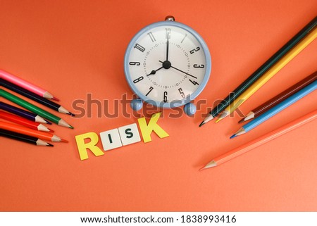Block letters on risk with alarm clock and colorful pencils on orange background 