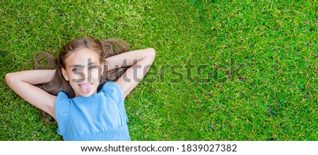 Happy teen girl lying on grass, top down view. Empty space for text