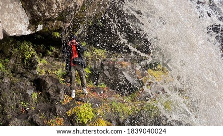A photographer stands under a beautiful waterfall and takes pictures. Stunning autumn landscape. Beautiful place. Travel to the Kamchatka Peninsula.