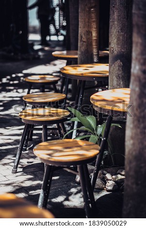 Vertical atmospheric warm summer cover photo, wooden stools chairs in outdoor cafe on veranda in garden, bright rays sun beam through trees. Positive good calm mood concept, for wallpaper screensaver
