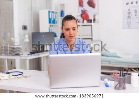 Medical practitioner typing patient health report on laptop in hospital office. Health care staff sitting at desk using computer in modern clinic looking at monitor, medicine.
