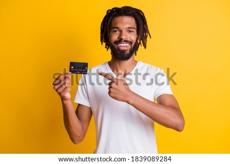 Photo of black beard dreadlocks guy indicate finger hold credit card wear white t-shirt isolated yellow color background