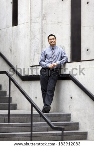 Stock photo of a Hispanic businessman leaning against a wall running alongside a stairwell.