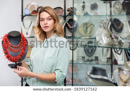 Portrait of happy young woman demonstrating natural coral necklace in jewelry shop Royalty-Free Stock Photo #1839127162