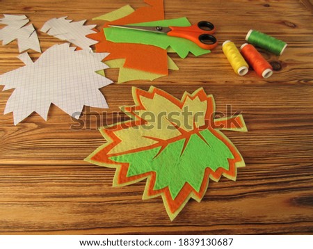 Bright autumn leaf and colorful threads on a wooden table. Decorative maple leaf is made of felt. Creative idea.