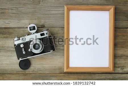 Directly above the shot of a blank frame with a retro camera on an old wooden table.	

