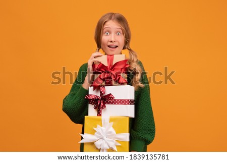 Image of charming blonde girl 12-14 years old in warm green sweater holding a lot of gift boxes. Studio shot, yellow background, isolated. New Year Women's Day Birthday Holiday concept