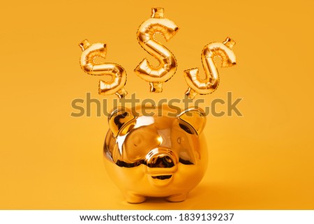 Golden piggy bank on yellow background with Gold USD Sign Balloons. Golden currency symbol made of inflatable foil balloon. Investment and banking concept.Money saving, moneybox, finance, investments.