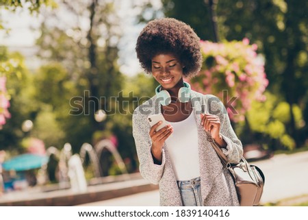 Photo of positive dark skin girl read social media news on cellphone in green town center park with trees