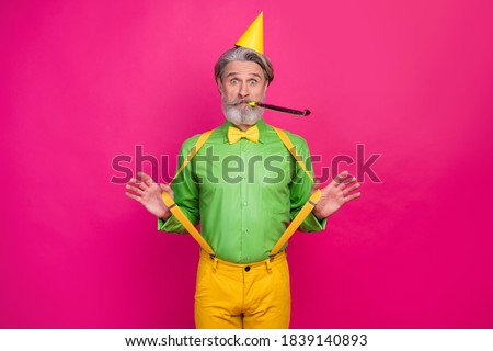 Photo of funny white haired grandpa hold yellow suspenders blow noisemaker funky crazy birthday party surprise wear paper cap green shirt pants isolated bright pink color background