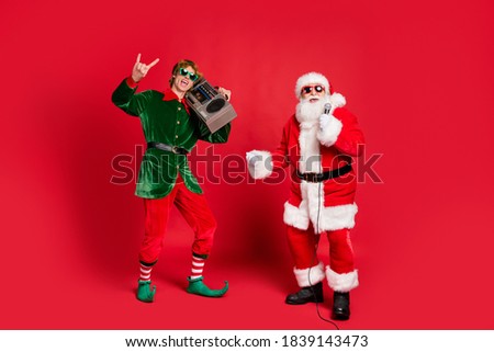 Photo of two crazy men elf hold boom box show horns santa sing mic wear sunglass x-mas costume coat hat isolated red color background