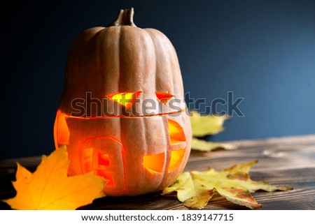Spooky Jack-shaped pumpkin for Halloween with cut-out eyes, Windows and door and a flickering candle inside. Orange lantern for a holiday on a dark background, space for text