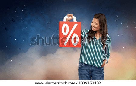 sale, outlet and consumerism concept - happy asian young woman with percentage sign on red shopping bag over night sky and stars on background