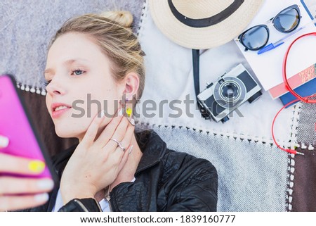 Beautiful woman makes a selfie in the park. Woman lying down takes a picture. Portrait of a blonde woman with blue eyes.
