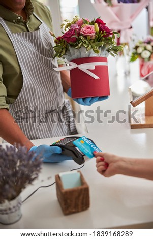 Cropped photo of a multiethnic male florist standing with a bunch of roses while withdrawing payment from client debit card
