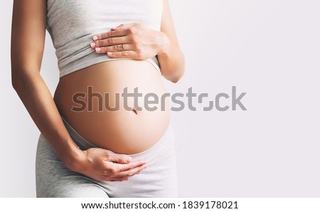 Pregnant woman holds hands on her belly on white background, close-up. Beautiful photo of pregnancy. Mother waiting for baby. Women prepare for maternity. Concept of prenatal period, maternal health. Royalty-Free Stock Photo #1839178021