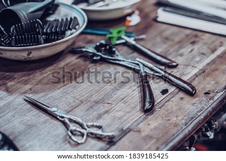 Arrangement Professional hairdressing barberian grooming Barbershop tools accessories for haircut, Scissors razor lying on wooden shelf table background retro barber shop salon. Vintage toned photo