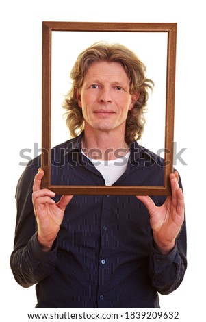Man holds an empty wooden frame in front of his face