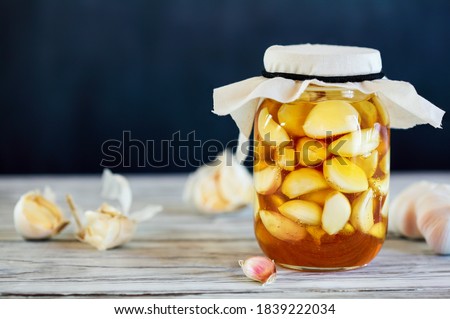 Fermented garlic cloves in a jar of honey, a rich source of probiotics, over a rustic wood background table. Selective focus with blurred background and foreground.