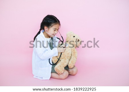 Little asia child girl dreaming about is a veterinarian using stethoscope with teddy bear on pink background Royalty-Free Stock Photo #1839222925