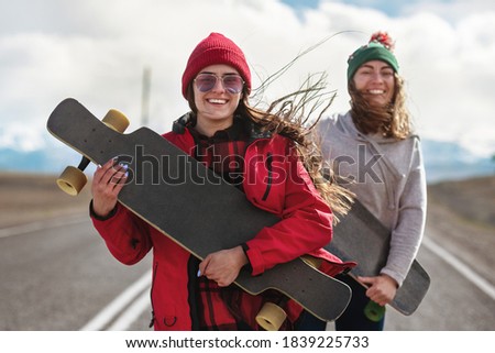 Two cheerful girls stands with long boards and having fun at the mountain road
