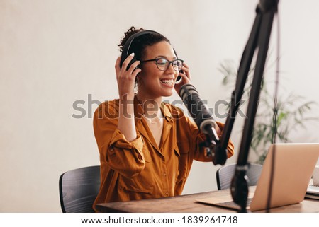 Woman wearing headphones preparing to record a podcast from home studio. Female working from home with a laptop and microphone on table.