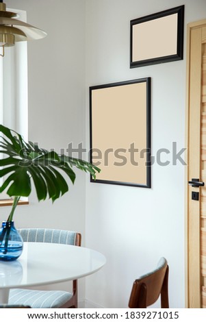 Stylish composition of dining room interior with design table, chairs, tropical leaf in vase,  mock up poster and elegant decoration in home decor.  Template.