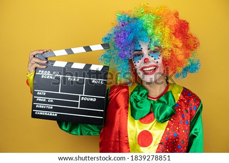 Clown standing over yellow insolated yellow background holding clapperboard very happy having fun