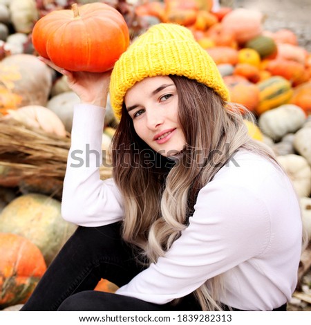 Teenager girl in woolen yellow hat posing at harvest farm and pumpkin patch
