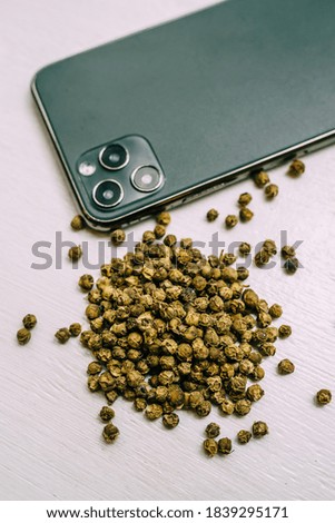 Dried green peppercorns are scattered on a white table near a mobile phone. Spices and condiments for cooking