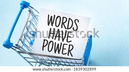 Shopping cart and text WORDS HAVE POWER on white paper note list. Shopping list concept on blue background.