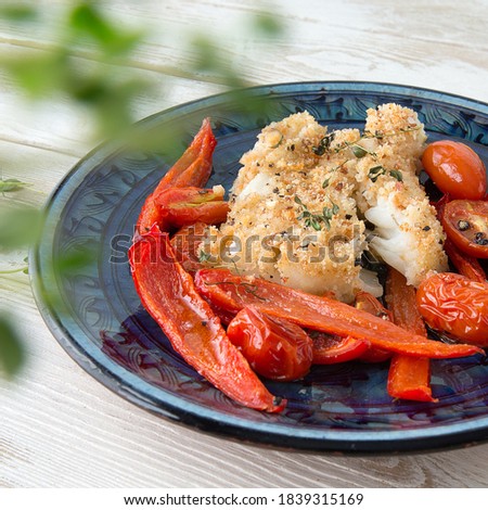 halibut fillet in bread crumbs with vegetables on a blue plate on a light wooden table