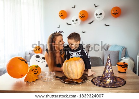 Happy family of mother and children prepare for Halloween pumpkins decorate the home. Mother with her son prepare pumpkin for halloween in the livingroom. 