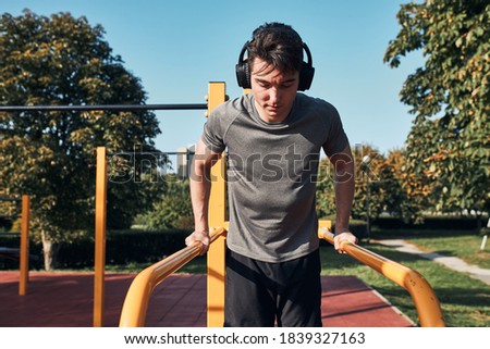 Young man doing dips on parallel bars during his workout in a modern calisthenics street workout park. Man listening to music wearing headphones and sportswear