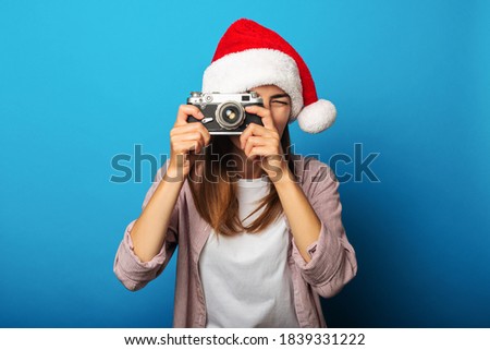 Young woman in santa claus hat takes pictures with retro camera