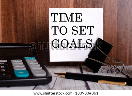 TIME TO SET GOALS is written on a white card on a wooden background next to a calculator and pen. Business Concept