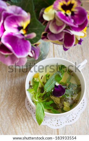 Glasses of green mint tea and vase with fresh violas on the table