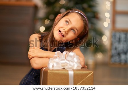 Happy childhood, Christmas magic fairy tale. Little girl dreams before opening Santa's present for Christmas.