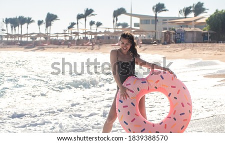 A cheerful woman with a doughnut-shaped swimming circle by the sea. The concept of leisure and entertainment
